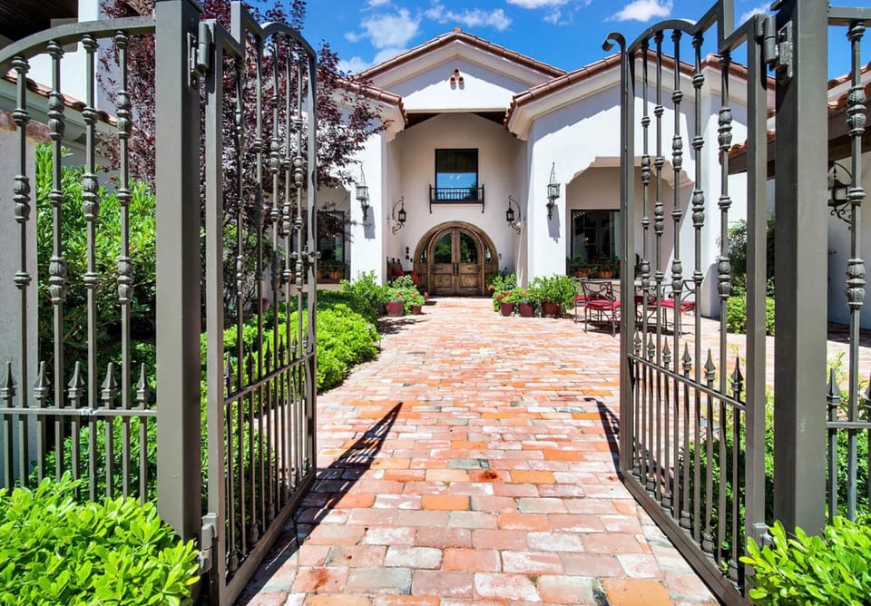 A planted entry court framed by iron gates and warm brick paving.