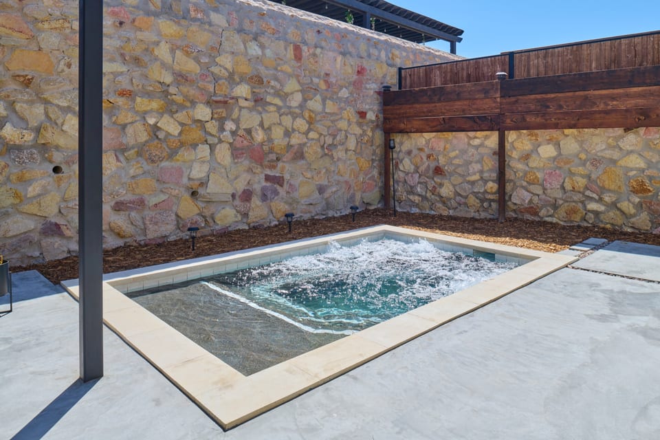 A compact pool enclosed by stone, timber, and a shaded steel structure.