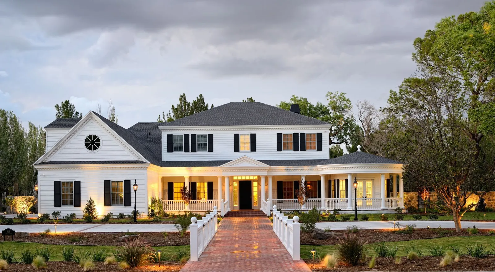 White two-story house with a porch and brick walkway, under a cloudy sky.