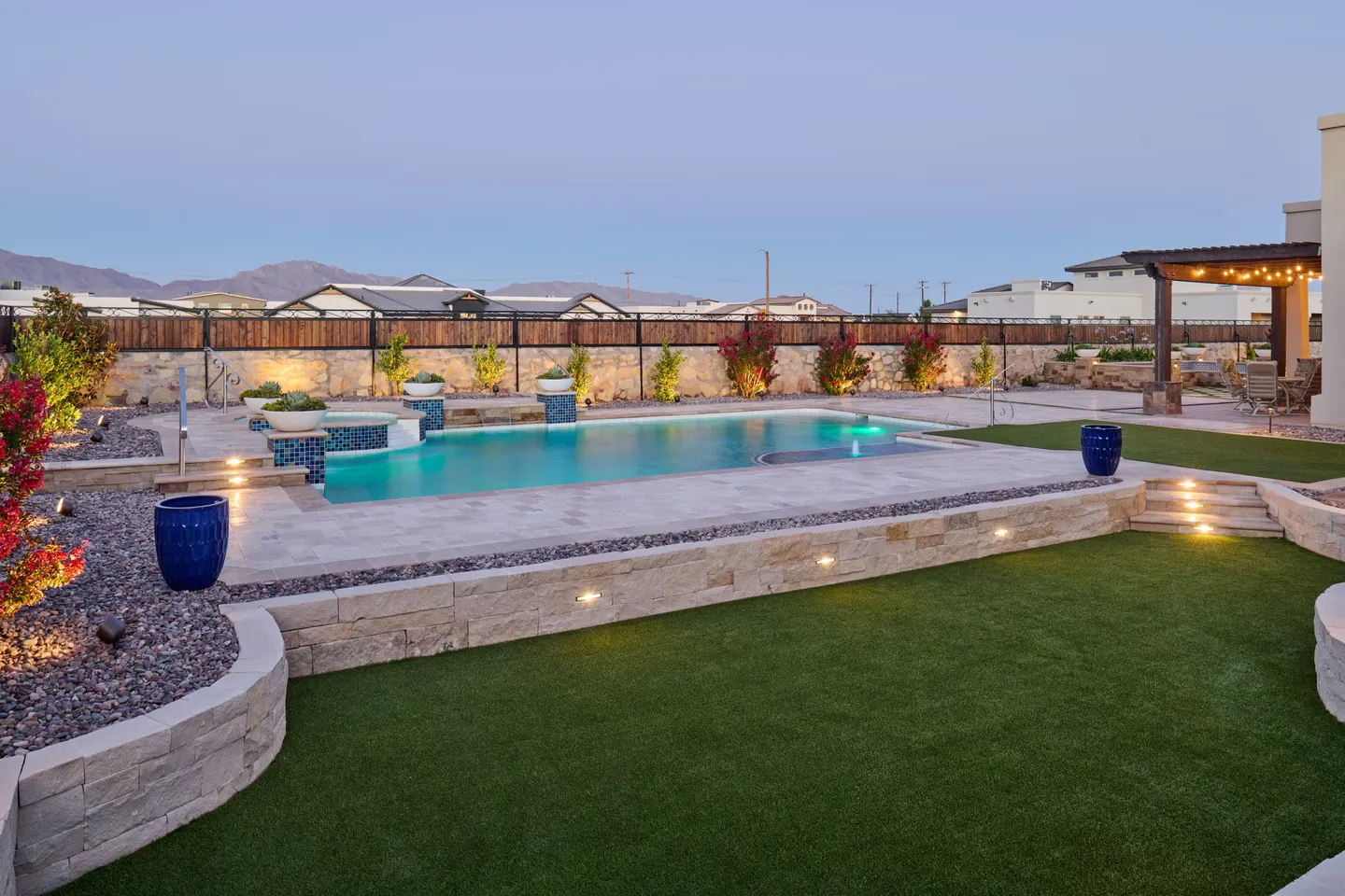 Backyard pool with stone features, steps, and landscaping at dusk.