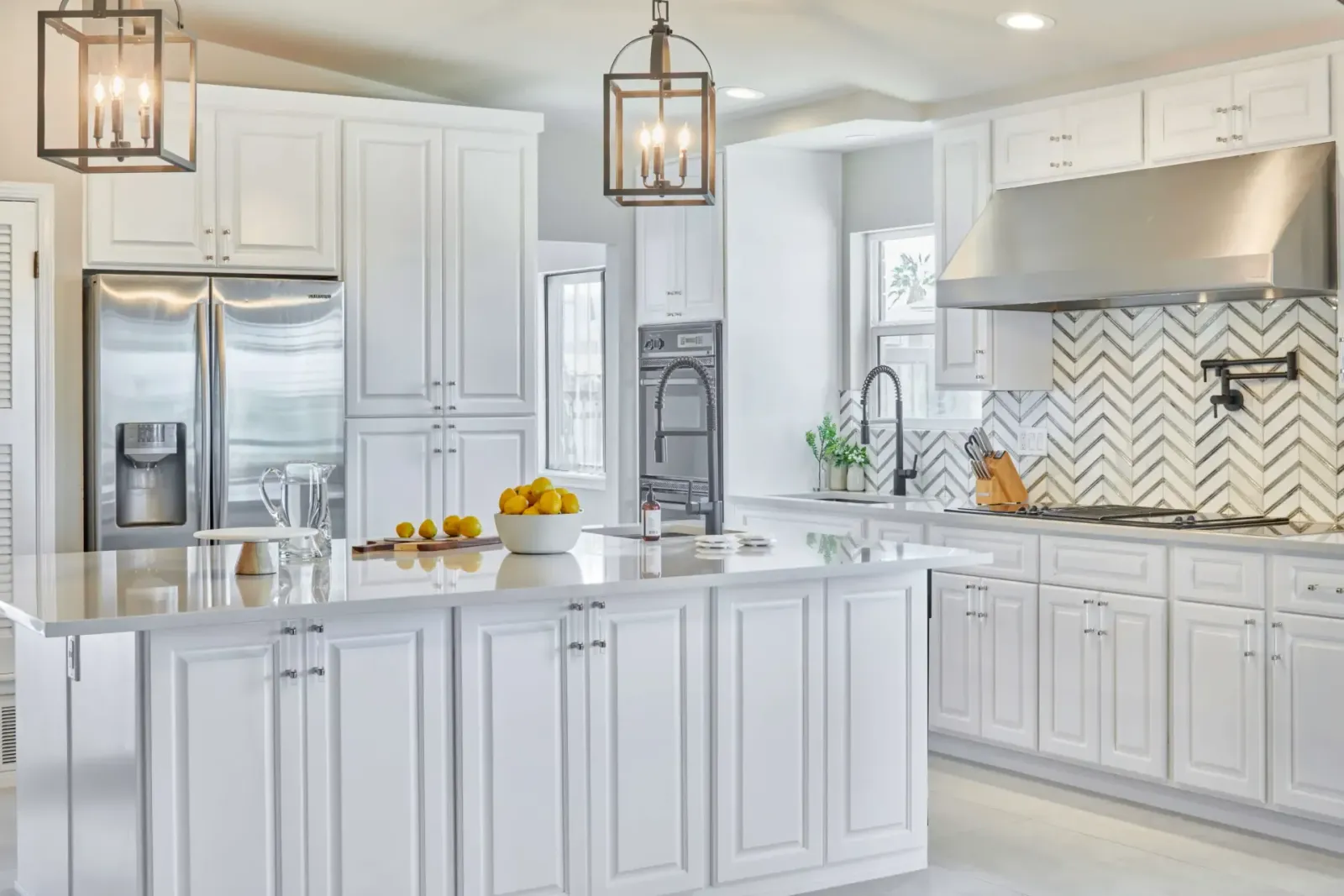White kitchen with island, stainless steel appliances, and herringbone backsplash.
