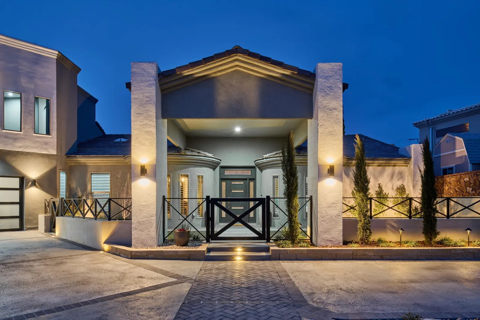 Modern house facade at dusk with lit pillars and landscaping.