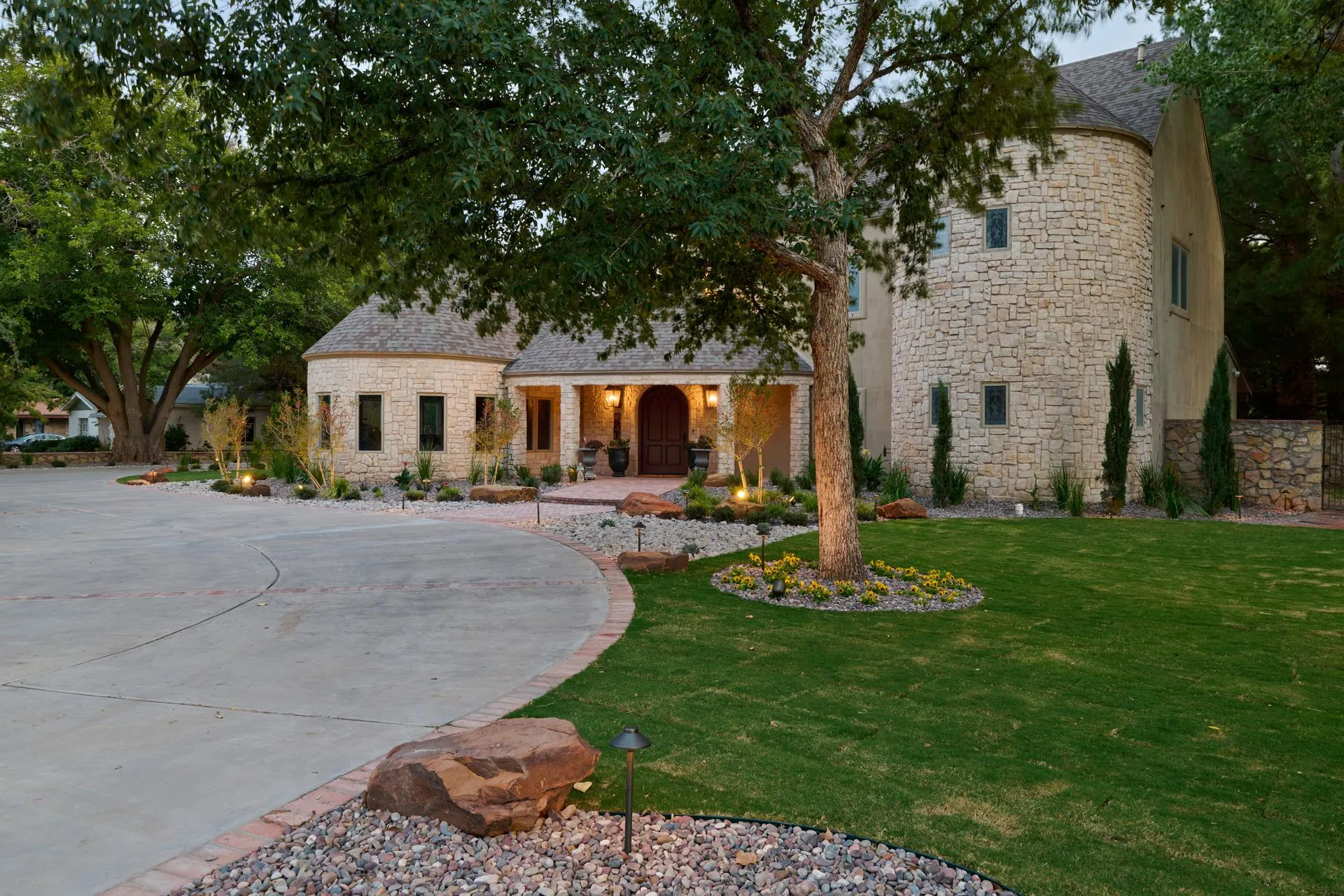 Stone house with circular tower, arched entryway, and landscaped front yard.