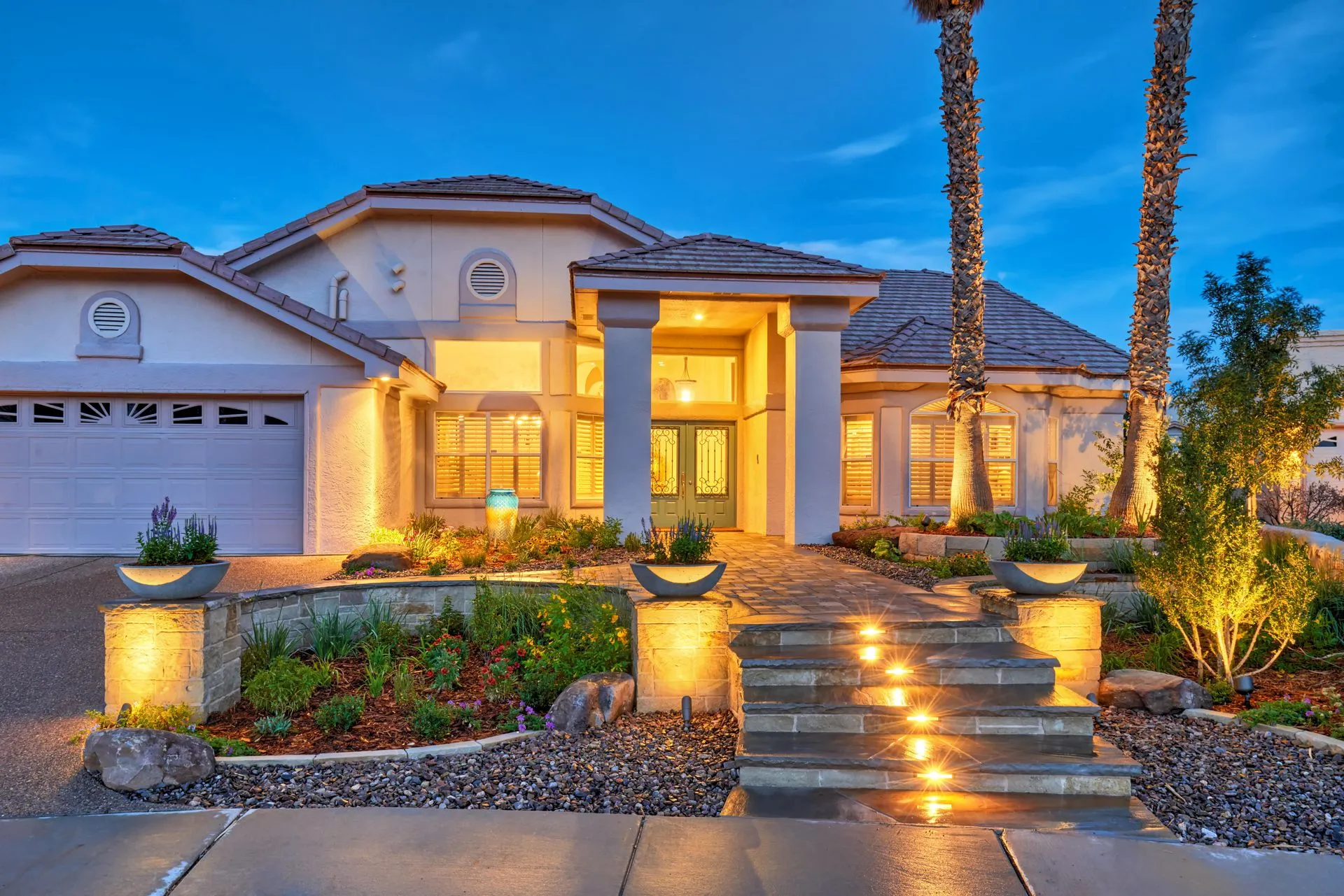 Elegant house exterior with illuminated steps, pillars, and landscaping at twilight.