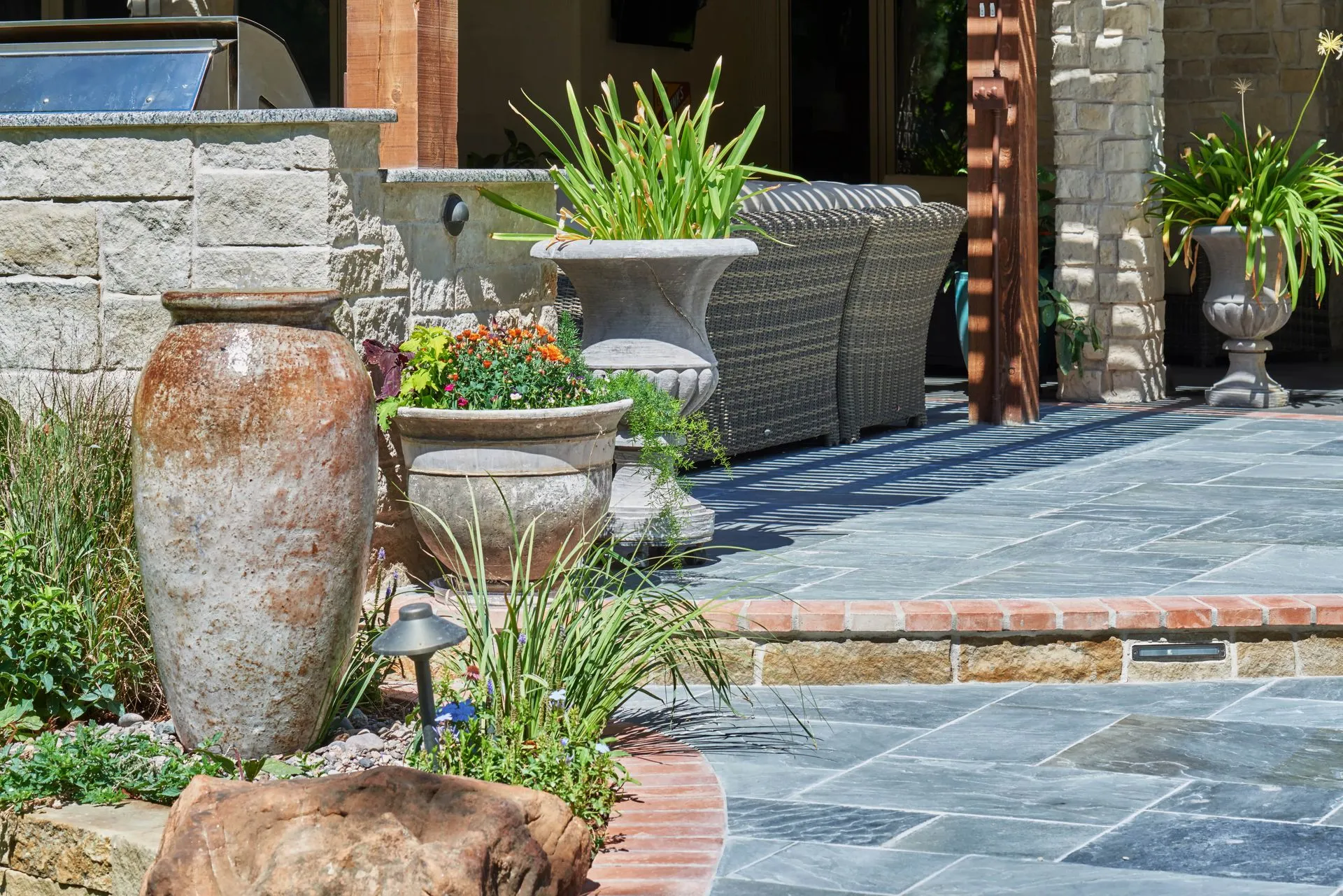 Outdoor patio with stone pavers, large pottery, and potted plants.