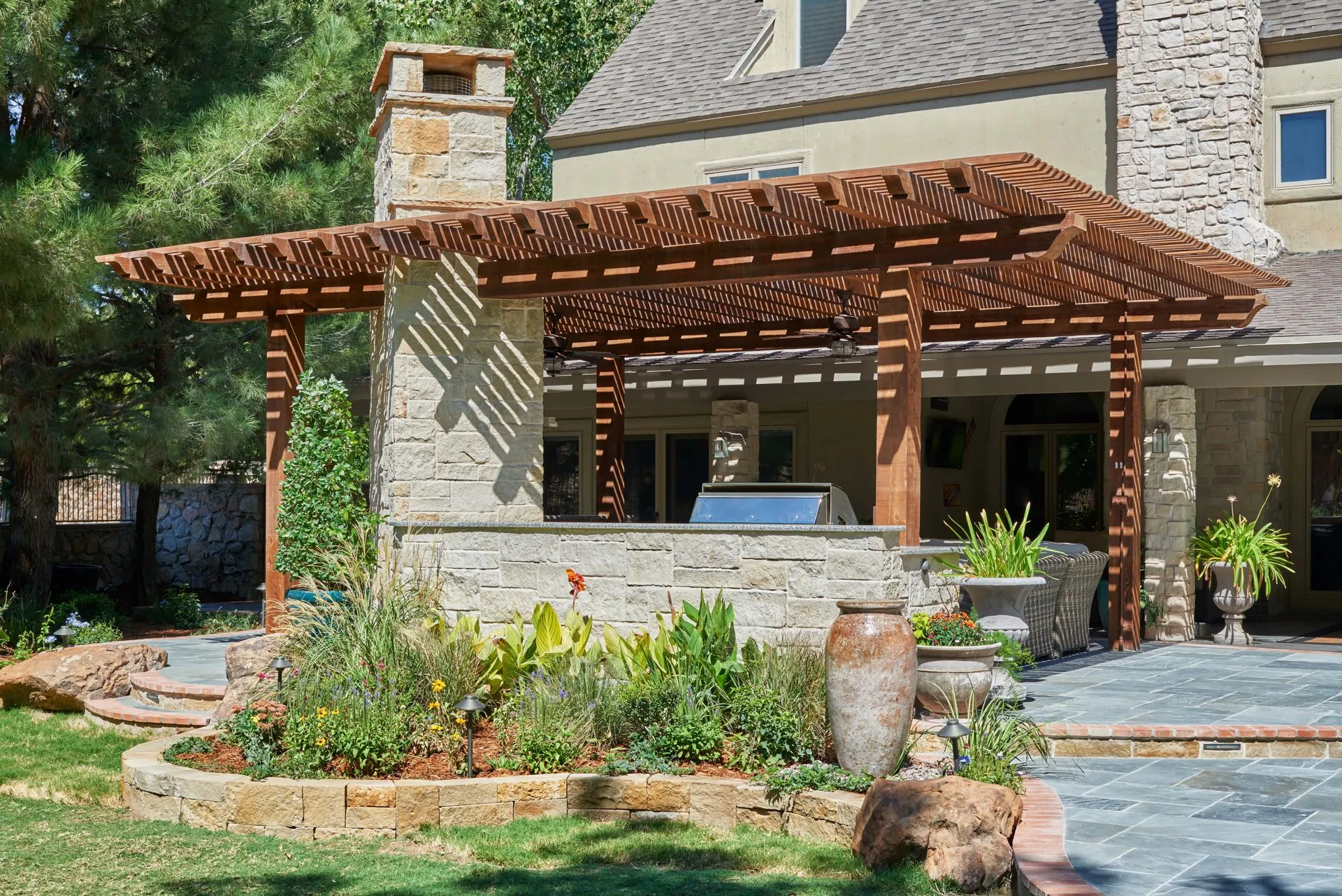 Wooden pergola over an outdoor kitchen with stone features, patio, and landscaping.