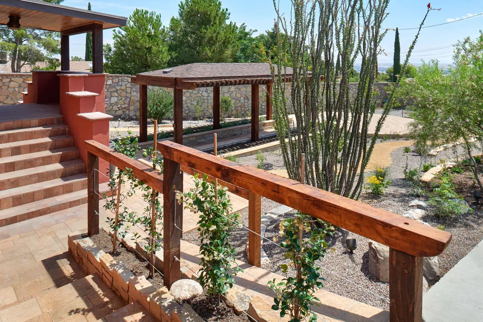 A planted garden with a wooden railing, stone steps, and pergola.