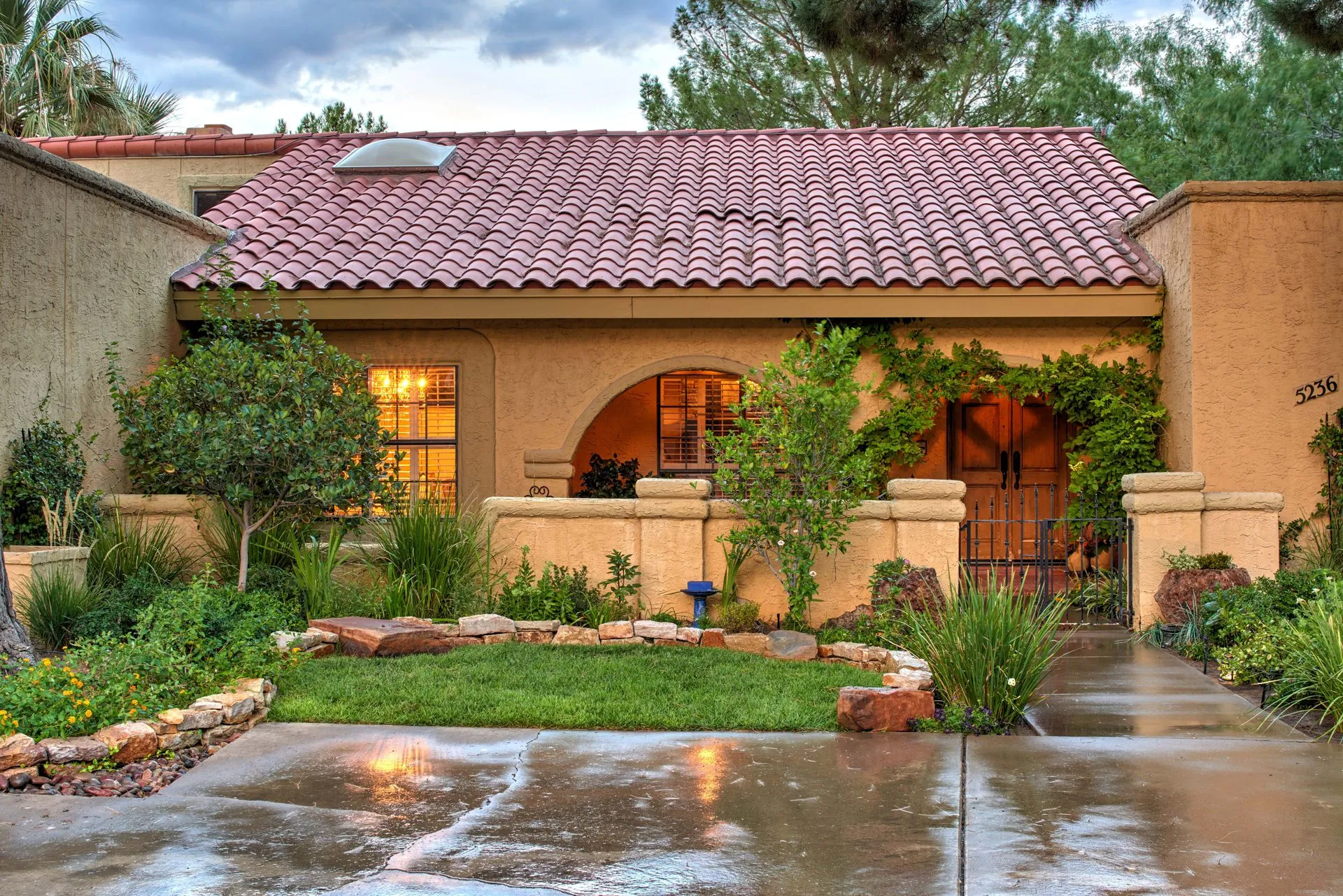 Spanish-style home with red tile roof, arched doorway, and lush landscaping.