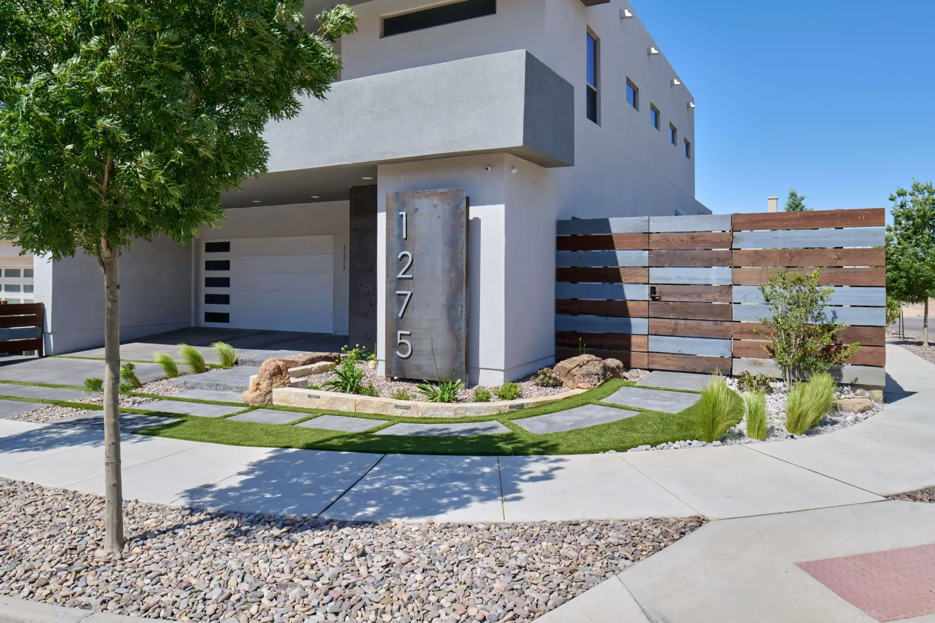 Modern two-story home with concrete accents, a landscaped front yard, and a wood privacy fence.