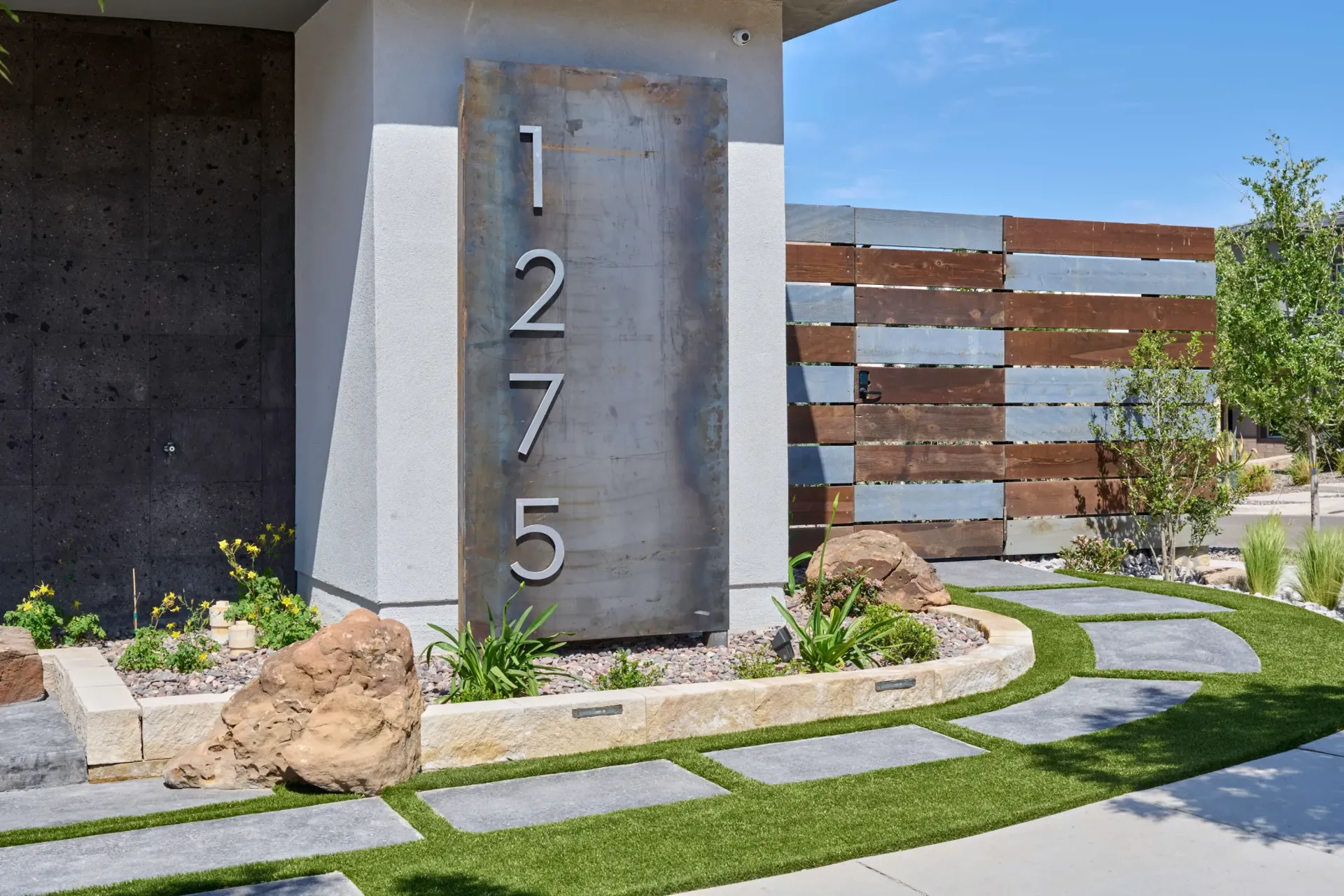 Metal house-number sign on a modern home facade beside a landscaped front yard.