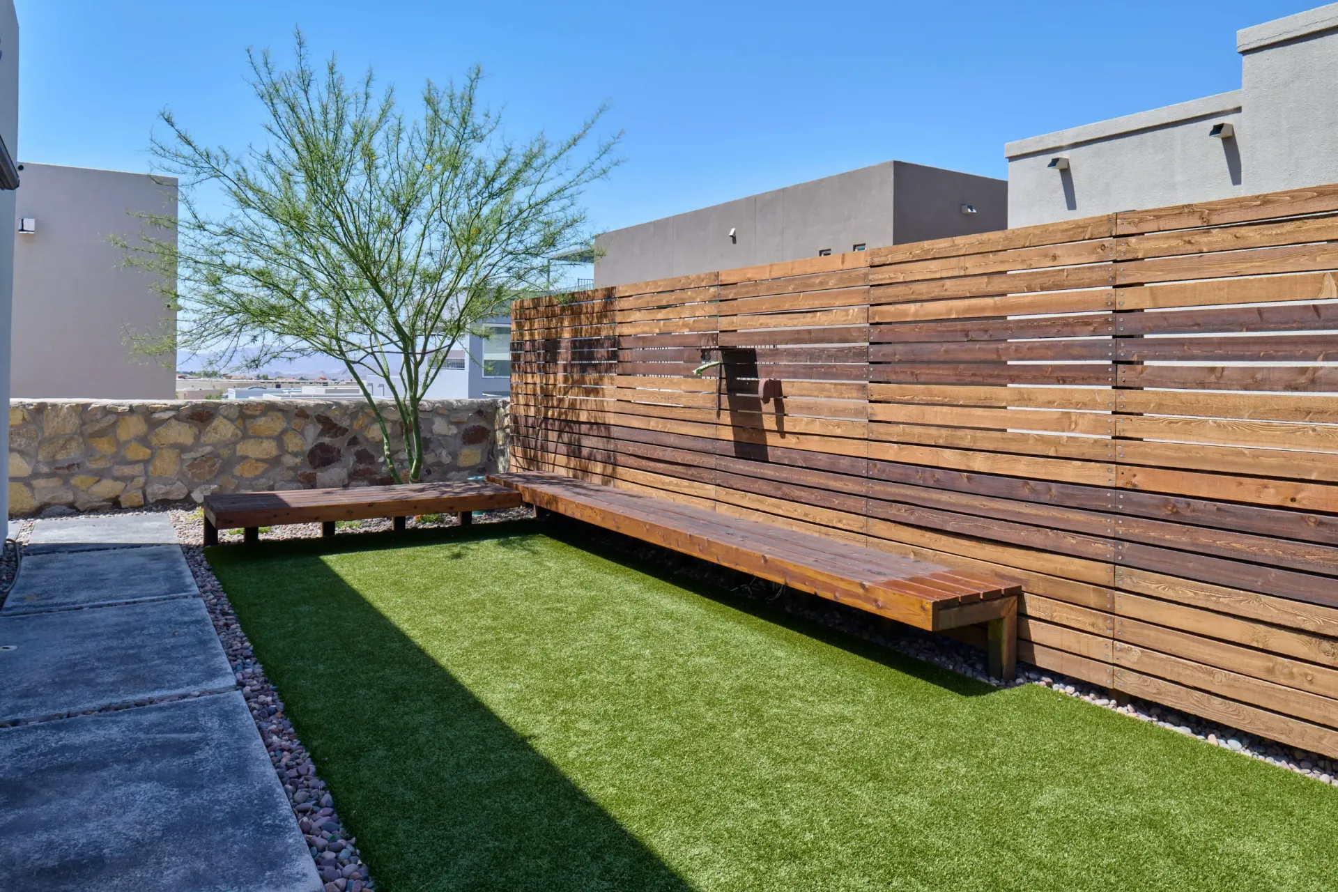 Courtyard with artificial turf, built-in wood benches, a tree, and a slatted wood fence.