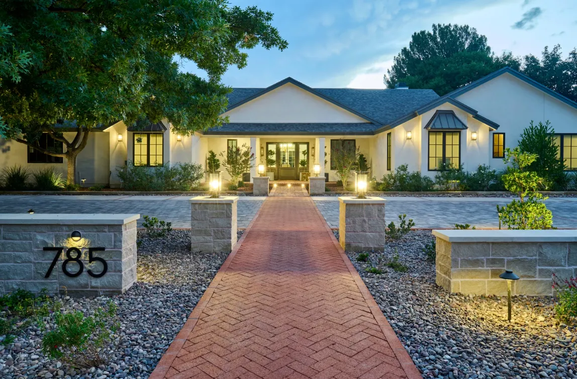 Brick path leads to a well-lit, white house with dark trim.