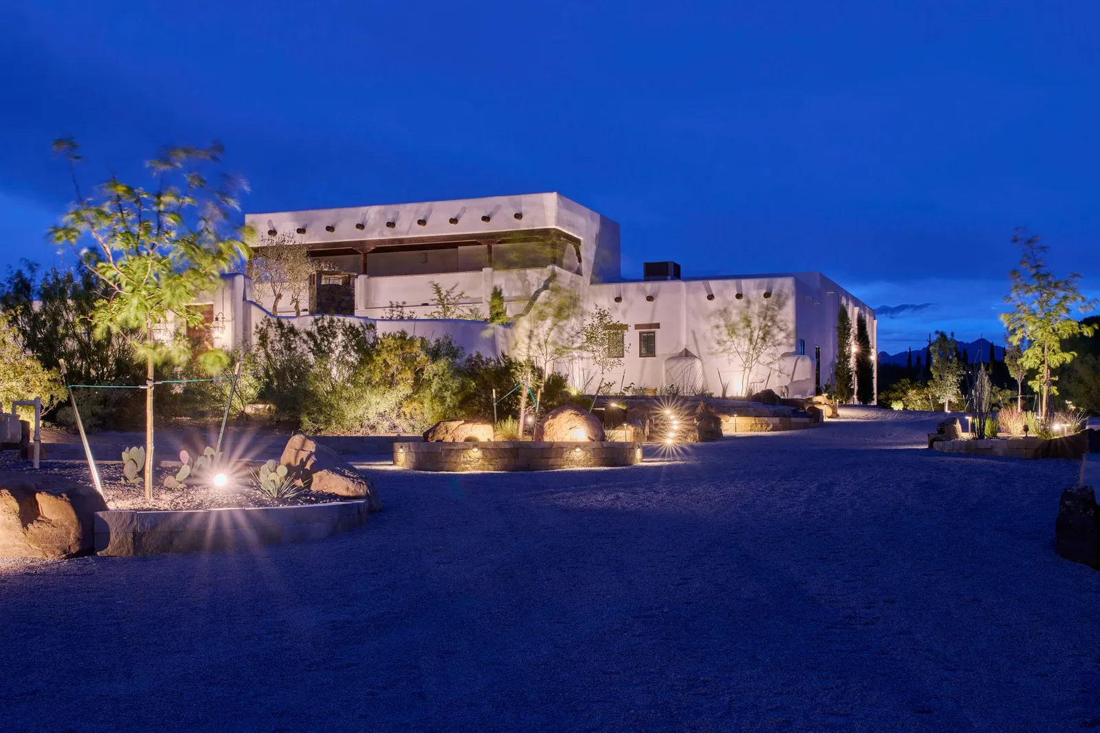 Modern stucco home illuminated at night with a gravel driveway and landscape lighting.