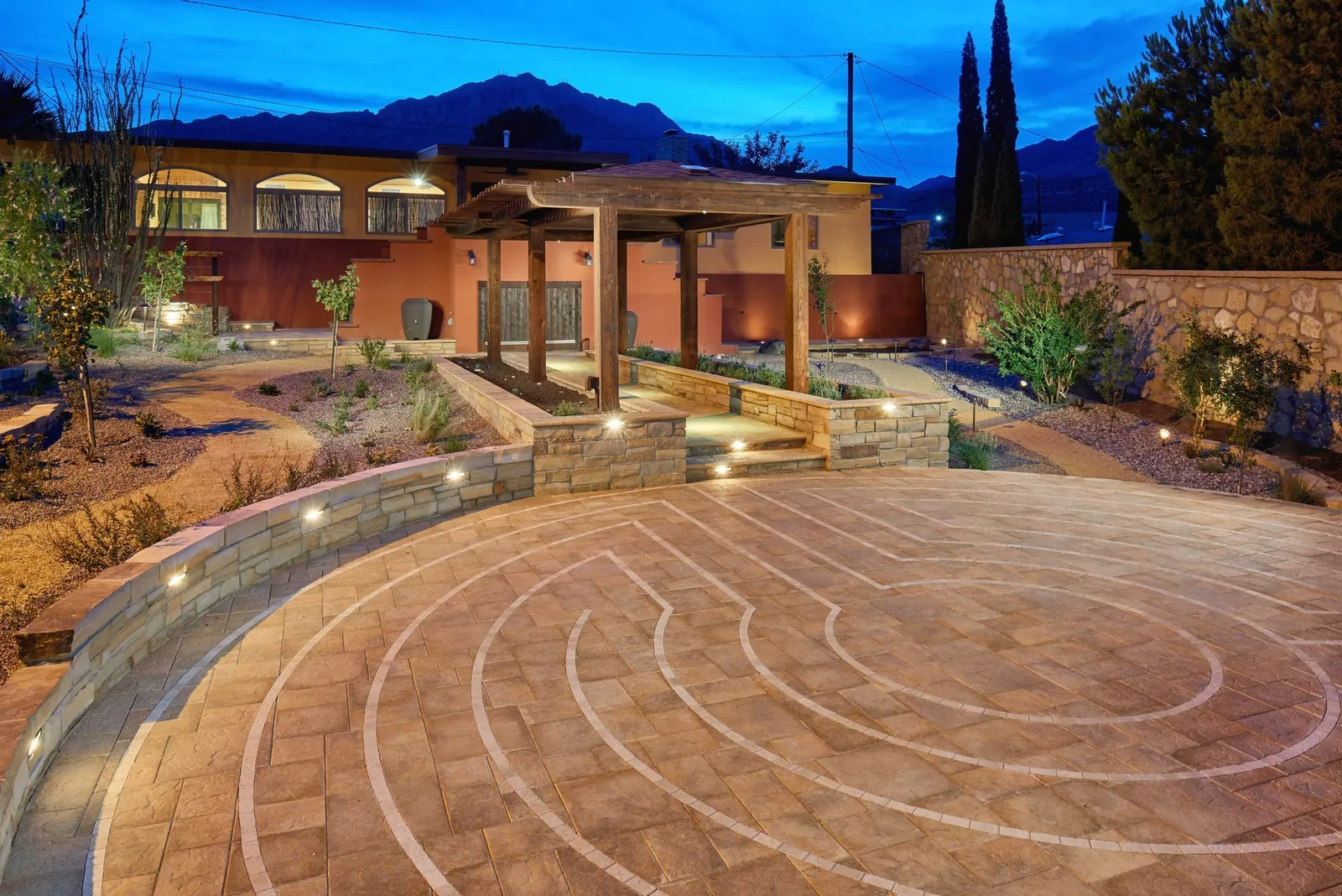 Circular patterned courtyard with a covered outdoor structure and mountain view at dusk.