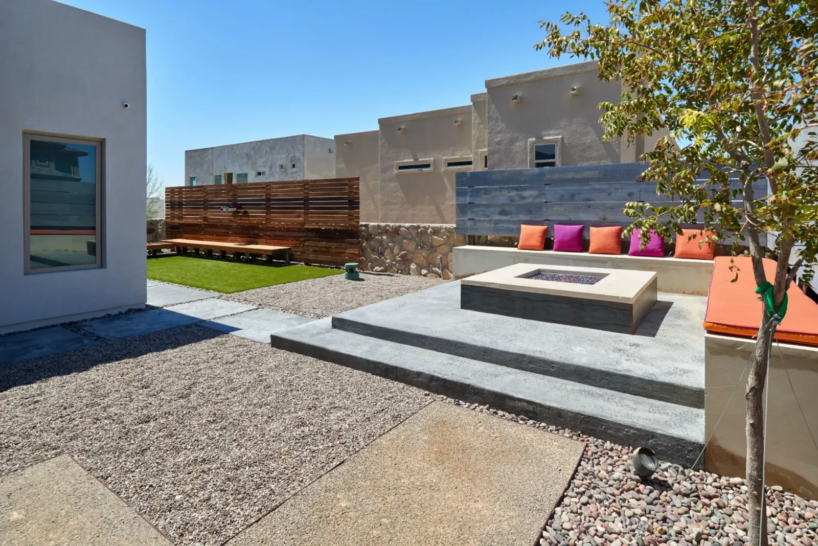Outdoor patio with fire pit, seating, and landscaping under a sunny sky.