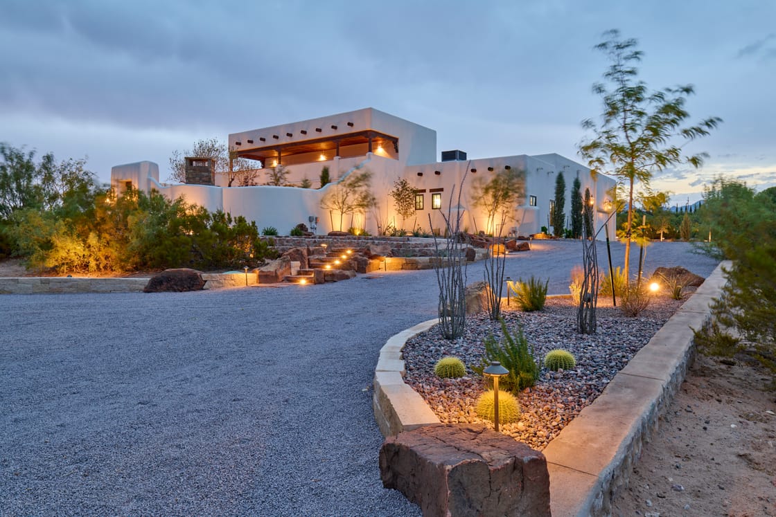 Low lights trace the curved edges of a gravel garden and planted stone beds at dusk.