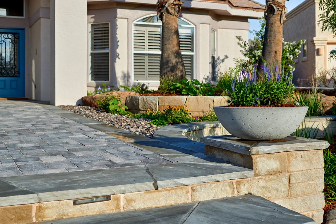A broad stone-paved entrance with raised planting and a large bowl planter.