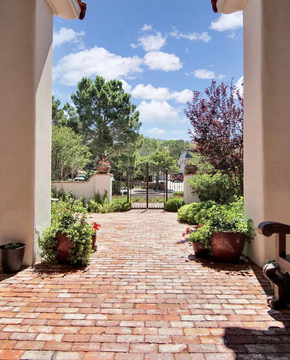 A brick path leads through a planted courtyard with low hedges and iron gates.