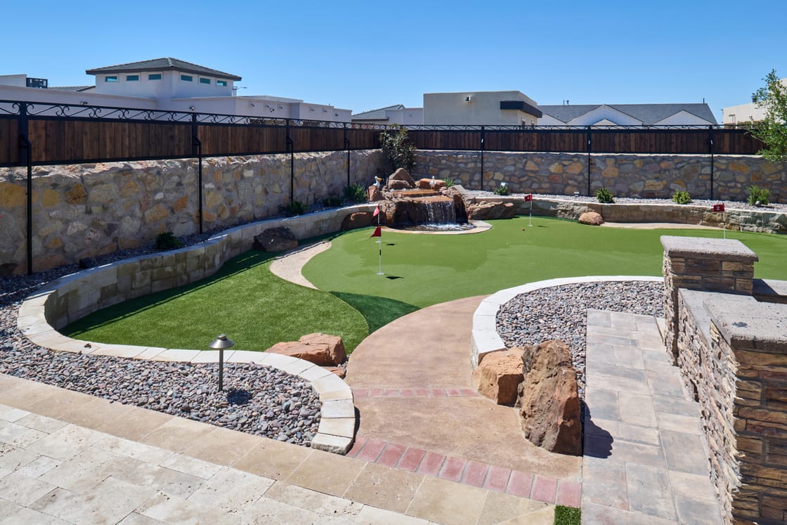 A putting green with a flagstick, curved stone borders, boulders, and gravel.