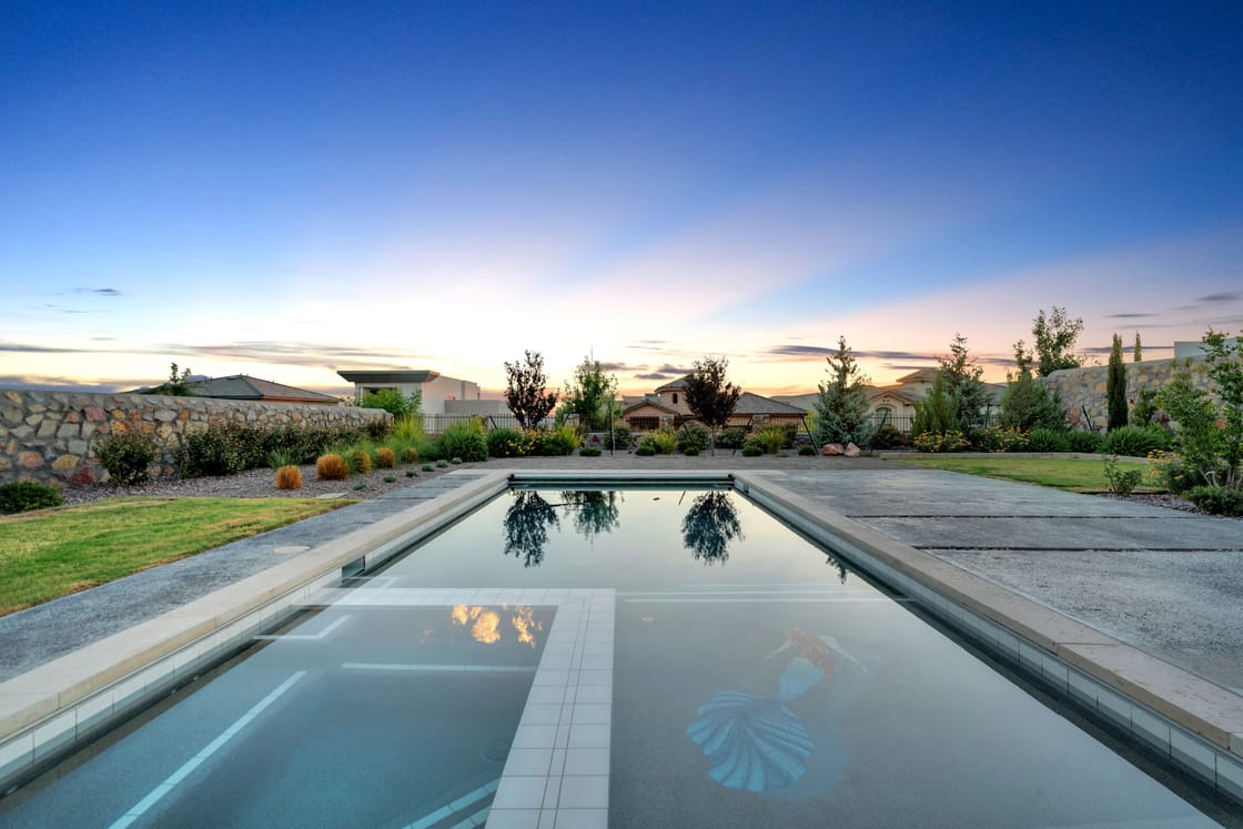 A long rectangular pool reflecting the evening sky beside a lawn and planted boundary.