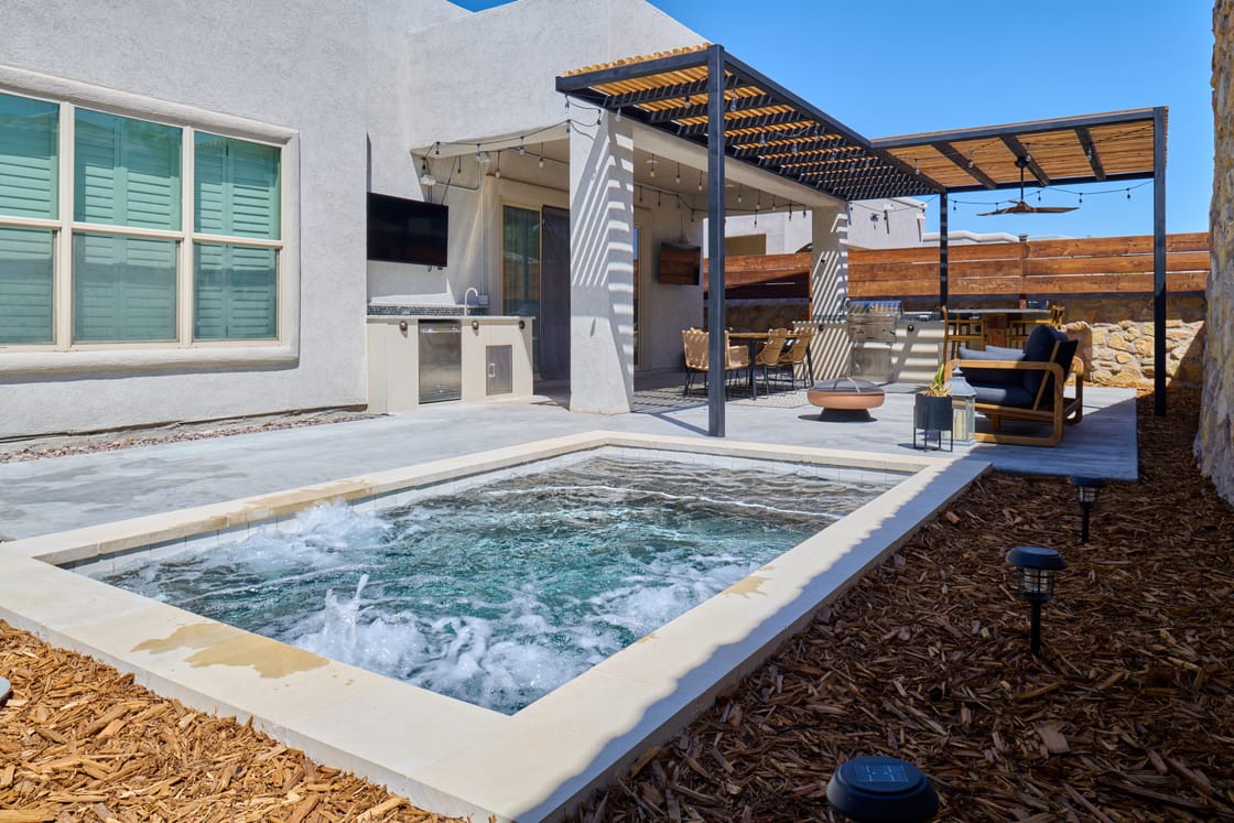 A compact pool with bubbling water beside a timber pergola and stone-walled patio.