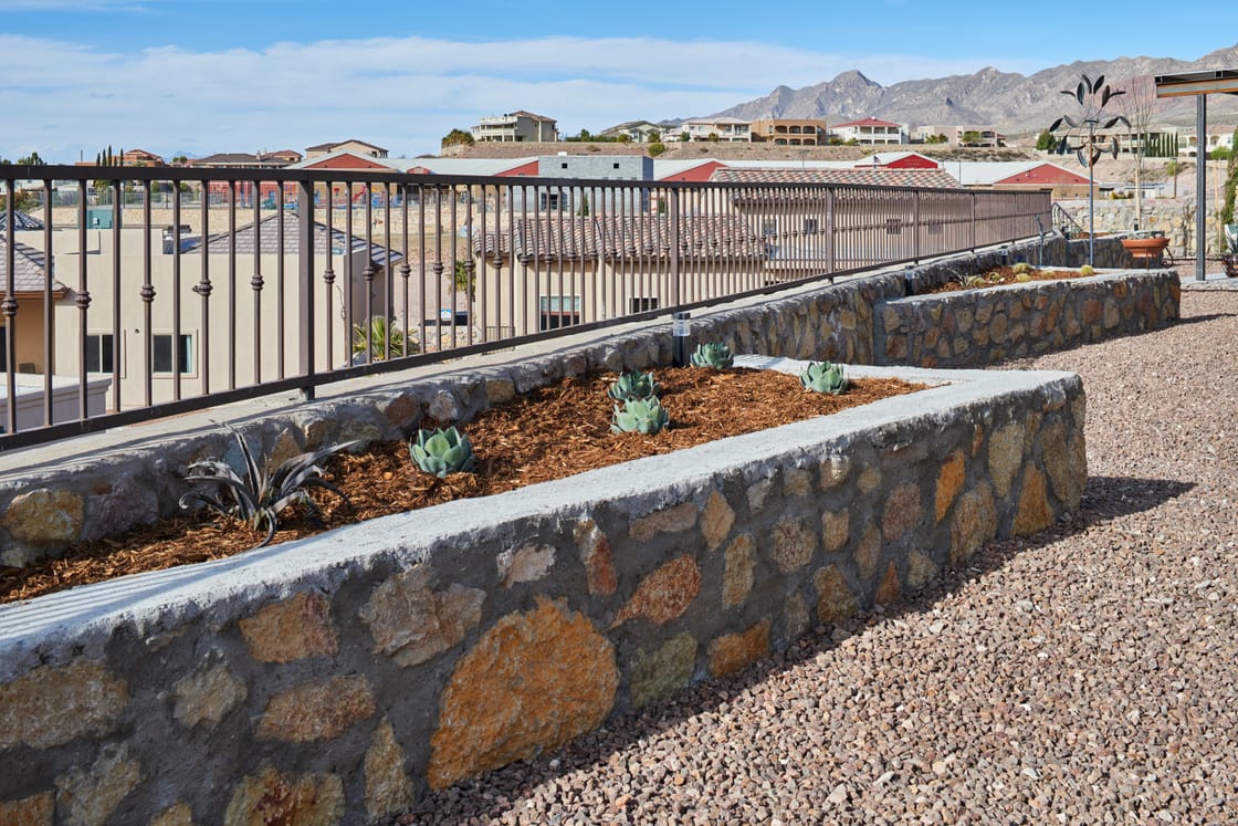 Terraced stone planting beds beside a gravel path and metal railing.